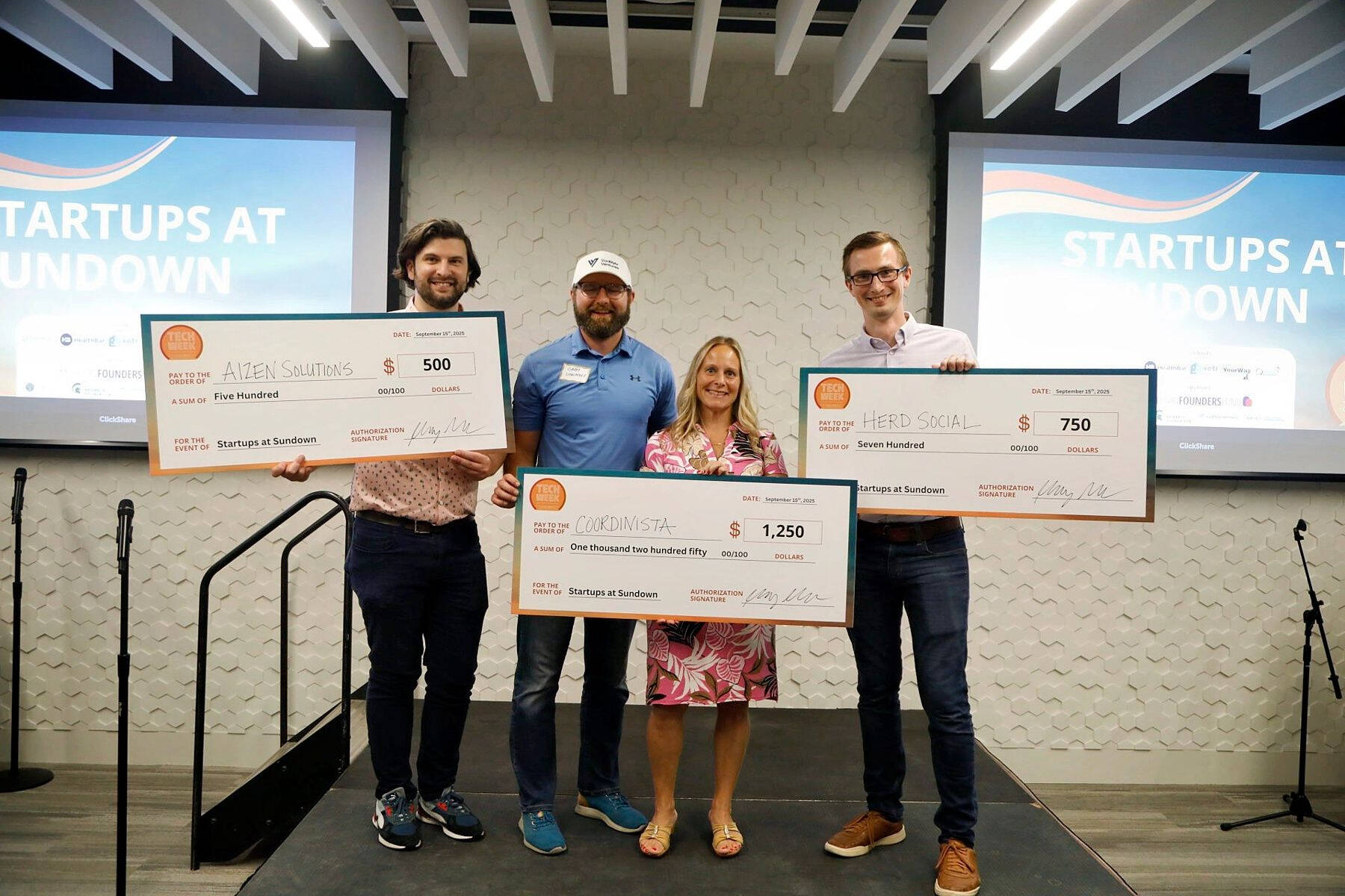 Dr. Zachary DeBruine (far right) holds an oversized $750 check for his startup, Herd Social, after winning second place at the Startups at Sundown competition during Tech Week Grand Rapids. He stands with other winners holding checks for their companies.